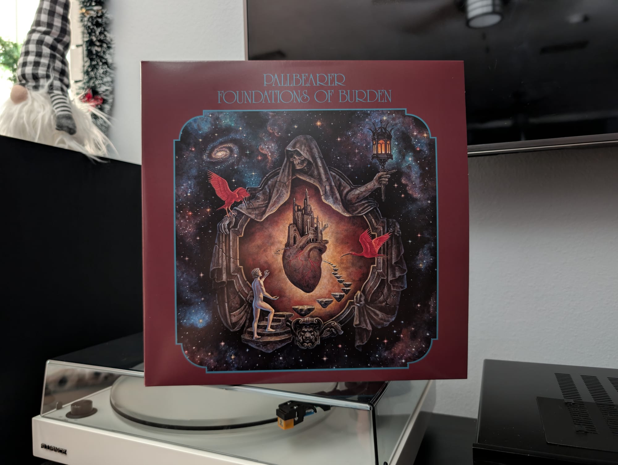 The Foundations of Burden record sitting on top of a turntable. On the cover is a death figure opening a path for an observer to walk to a floating heart with a castle on top.